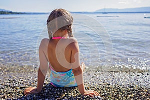 Girl has rest and sits on stones on pebble beach at Geneva Lake, summer vacations and travel