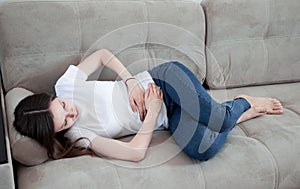 The girl has a stomachache. A woman lies on the couch, is sick, she has a stomach ache. Abdominal pain