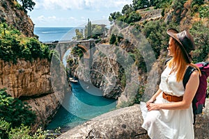 A girl in a hat with a backpack enjoys an incredibly beautiful view of a stone bridge over the gorge Fiordo di Furore. Little bay photo