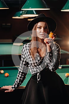 A girl in a hat in a billiard club with balls in her hands.Playing pool