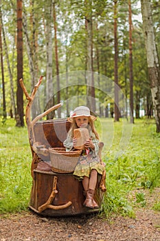 Girl in hat and dress rustic and boots sitting on a tree stump in the woods with a basket of bread and buns