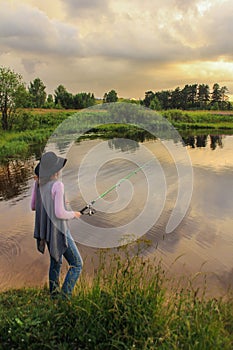 Girl in a hat fishing rod on the lake, summer landscape, storm clouds in the sky. outdoor activities. rear view