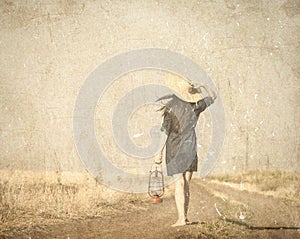Girl in hat with lamp waking on the contryside road
