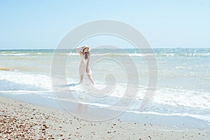 Girl in a hat and pink dress stands on the waves of the sea