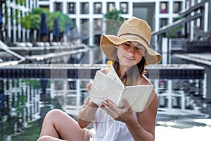 Girl in a hat reading a book by the pool