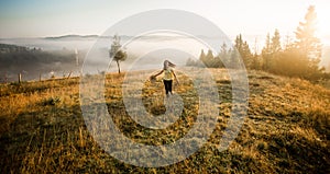 Girl with hat run with happiness on top of a mountain in autumn sunrise.