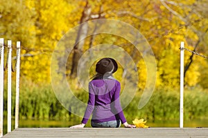 Girl in a hat sits on the dock and admires the colors of autumn.