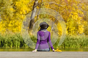 Girl in a hat sits on the dock and admires the colors of autumn.