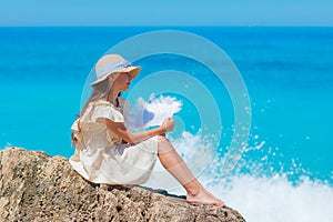 A girl in a hat sits on a stone by the sea