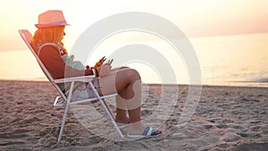 A girl in a hat sits on a sun lounger and works on a tablet pc