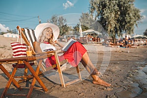 Girl with hat sitting on deck chair and reading book