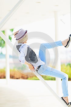 Girl in hat sitting on urban structure and looking into distance