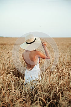 The girl in a hat stands in a field of ripe wheat in the sunset light. Sunset sun. Walking in the wheat field