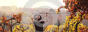 Girl in a hat at sunset and a glass of wine in hand. Nature Italy, hills and grape fields the sunlight. Glare and sun rays in the