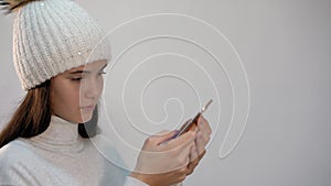 Girl in hat surfs internet with phone on light background