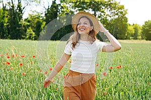 Girl with hat walking in a field with red flowers. Summer landscape. Warm colors. Woman walking through a poppy field. Young girl