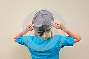 Girl in hat. White middle aged woman stays back to us and touches her hatâ€™s flaps. Back view with no face