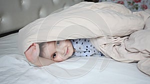 Girl having fun in a bed, she play with blanket, hide and scare adults