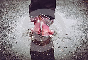 Girl having fun  jumping in water puddle on wet street  wearing rain boots with reflective detail fabric stripes shining.