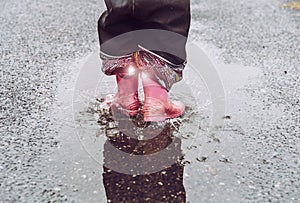 Girl having fun  jumping in water puddle on wet street  wearing rain boots with reflective detail fabric stripes shining.