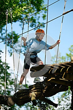 Girl having fun at outdoor extreme adventure rope park. Active childhood, playing outdoors.
