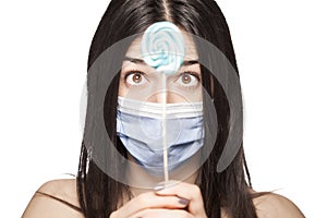 Girl having her mouth covered with with medical face mask holding lollipop