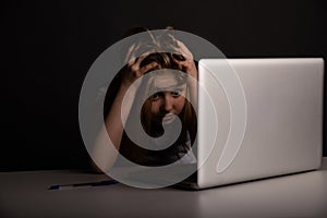 Girl with headache sitting at the desk and doing homework isolated. Tired child using computer.