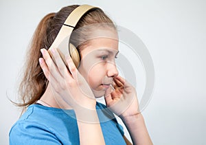 Girl in headphones and blue shirt listens to mp3 music. Child portrait with hands to head, side view