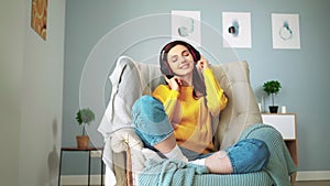 Girl in headphones with closed eyes relaxes on cozy sofa and listens music home
