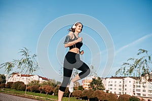 A girl in headphones is engaged in outdoor fitness in a metropolis. running and sports in summer