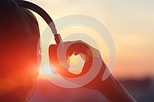 Girl in headphones listening to music in the city at sunset