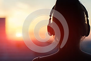 Girl in headphones listening to music in the city at sunset