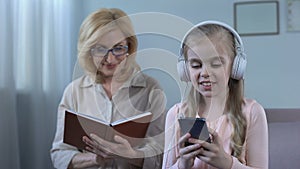 Girl in headphones listening to music and grandma reading book, generation gap