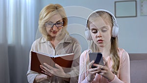 Girl in headphones listening to music and grandma reading book, generation gap