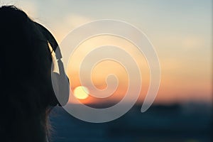 Girl in headphones listening to music in the city at sunset