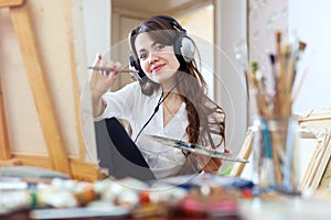 Girl in headphones paints on canvas in workshop