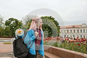 a girl with headphones and pink hair is traveling around the city with a backpack on her shoulders. Talking on the phone