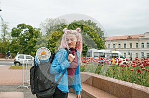 a girl with headphones and pink hair is traveling around the city with a backpack on her shoulders. Talking on the phone