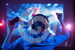 Girl in headphones plays a video game on the big TV screen. Gamer with a joystick. Online gaming with friends, win, prize. Fun