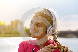 Girl in headphones and red shirt listens to mp3 music in city park. Teen portrait with hands to head backlight sun flare