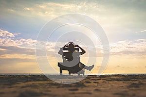 Girl in headphones is sitting on the sun lounger listening to music on the beach at sunset.
