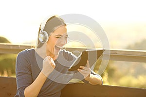 Girl with headphones and tablet celebrating at sunset