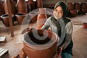 girl in headscarf smiles while making clay pots on wheels