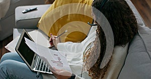 Girl in headset sits on couch and fills out documents, works on laptop, remote work from home, customer service office