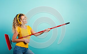 Girl with headset use the broom like a guitar. Cyan background