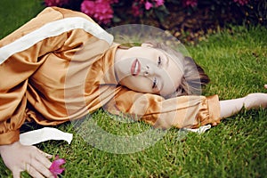 A girl with healthy beautiful hair lies on the grass and looks at the camera. Girl with perfect skin and natural care. Flower in