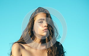 Girl with healthy young skin and bare shoulders. Woman with natural makeup on blue sky. Pretty woman with long hair