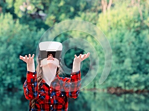 Girl in the helmet of virtual reality against the background of nature. Hands up. Tonning