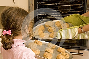 Girl helping mum bake cookies in oven