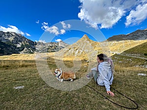 Girl with her bright red dog sitting on a hill high in the mountains